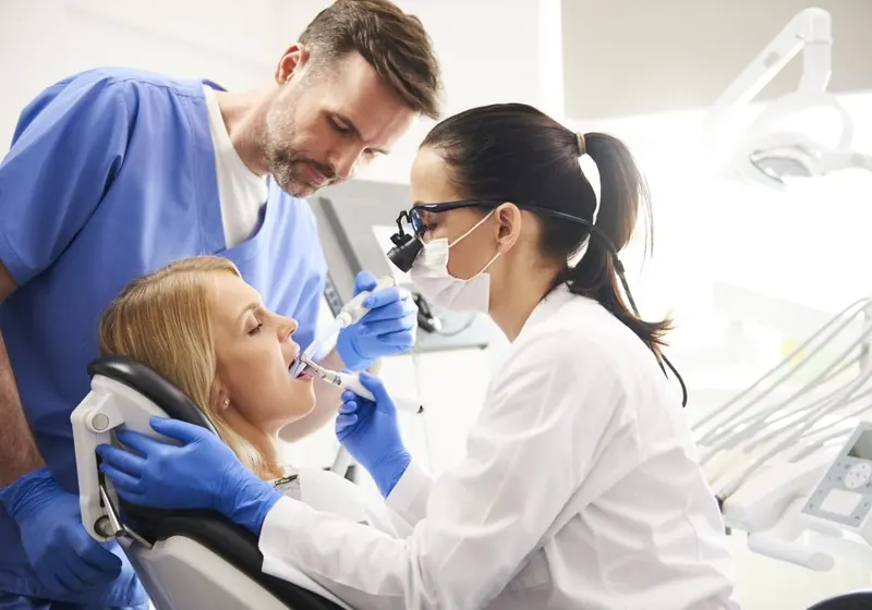 Dentista e auxiliar atendendo um paciente na OdontoSin